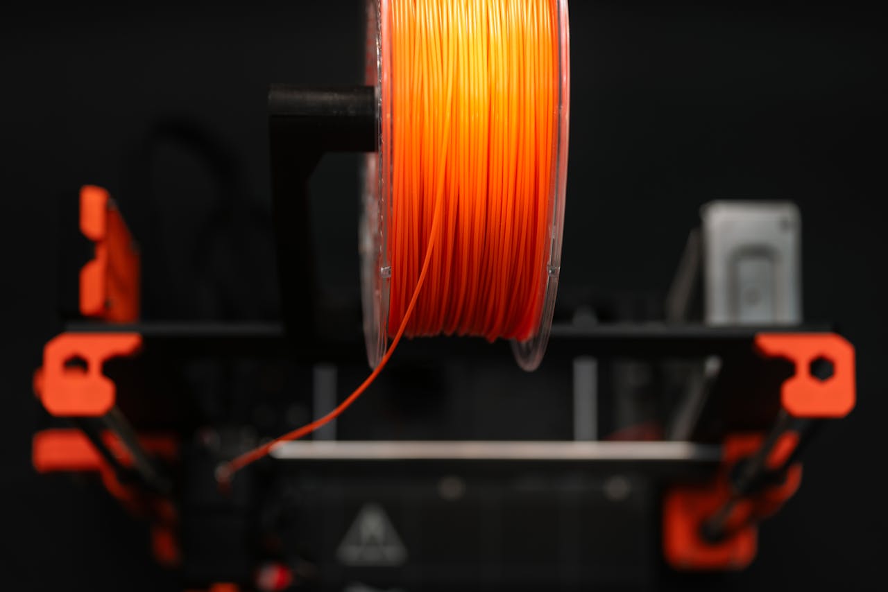 Close-up of an orange 3D printer filament spool in a workshop setting, highlighting innovation and design.
